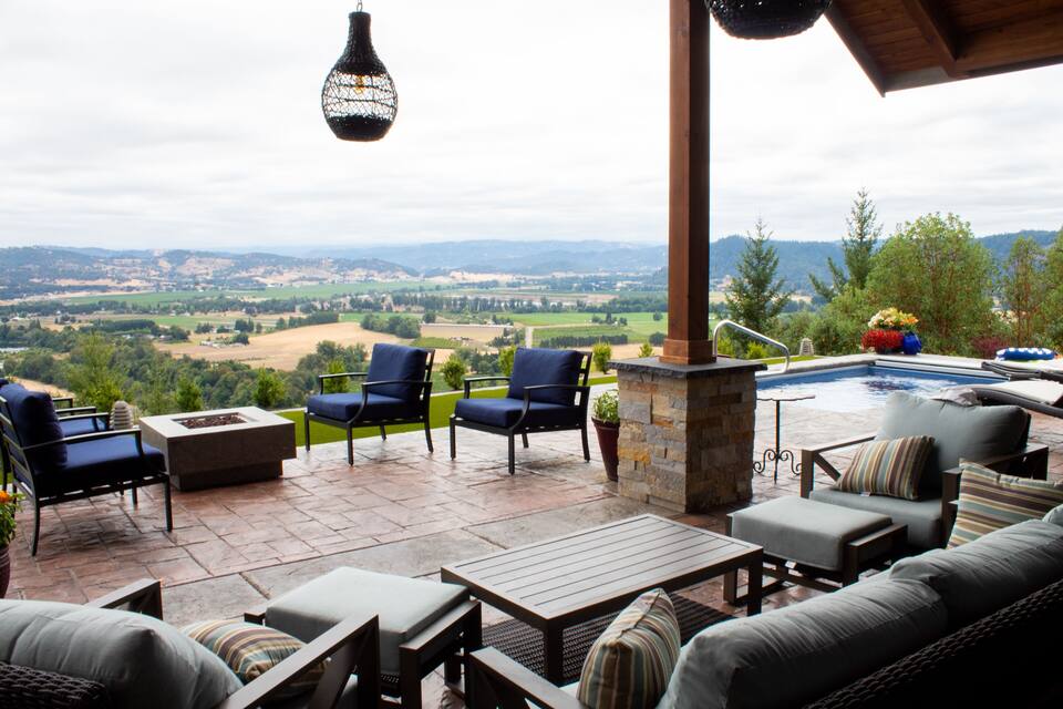 A patio with outdoor furniture overlooking a pool and a scenic view of a valley.
