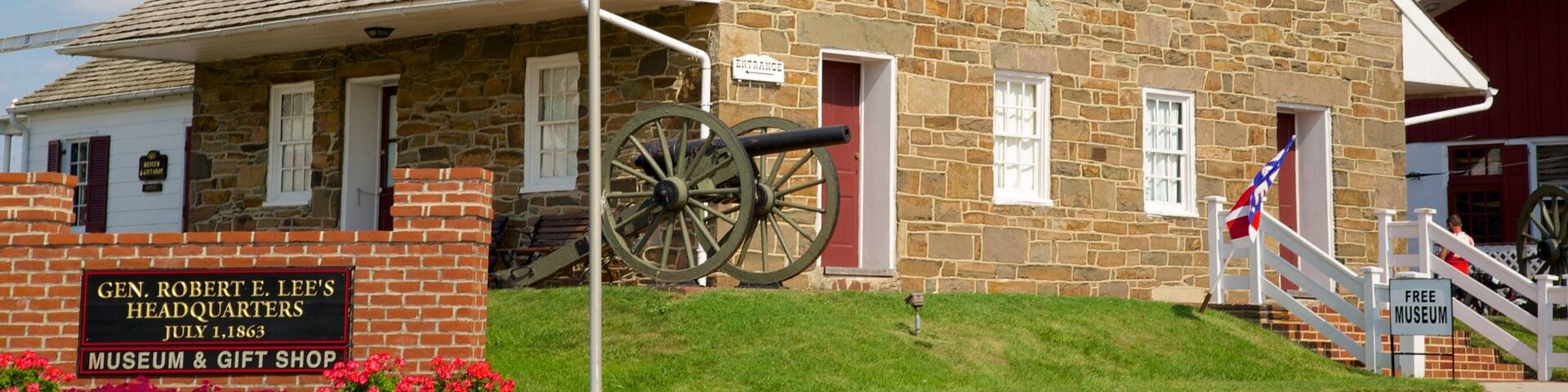A historic building with a stone facade, a flagpole with a flag, a cannon, and a sign indicating it's the Gen. Robert E. Lee's Headquarters Museum & Gift Shop.