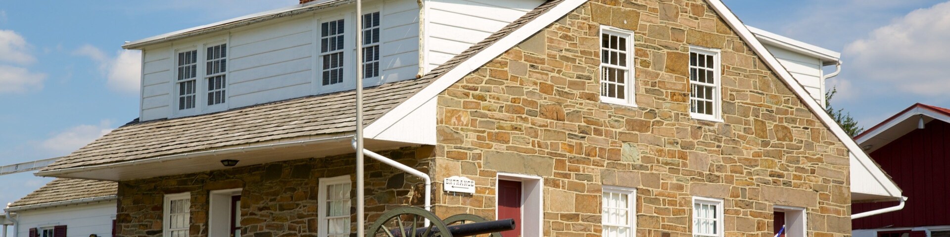 Um edifício histórico com fachada de pedra, mastro com bandeira, um canhão e uma placa indicando ser o Museu e Loja de Presentes da Sede do General Robert E. Lee.