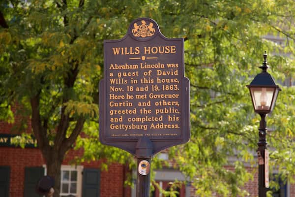 A historical marker sign for Wills House with a background of trees and a brick building.