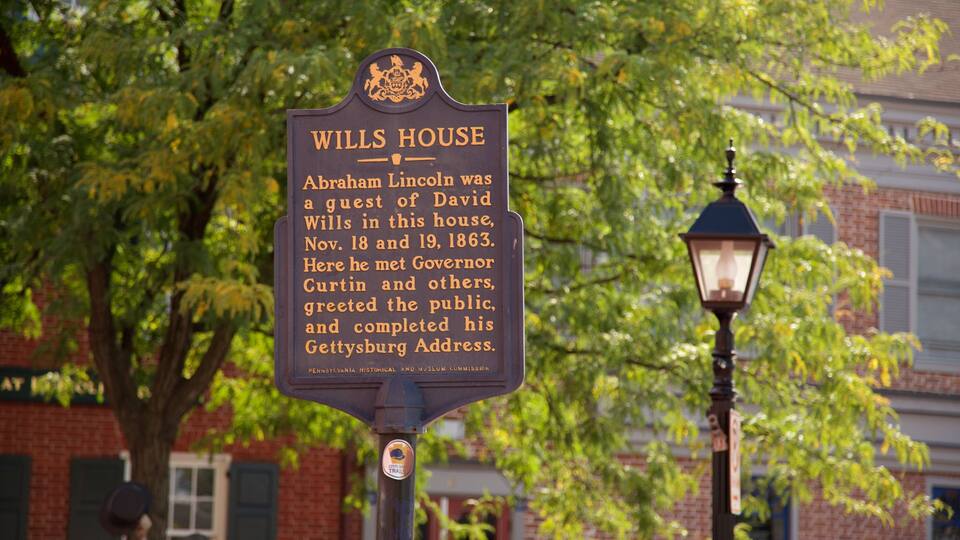 A historical marker sign for Wills House with a background of trees and a brick building.