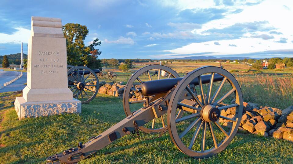A cannon, a monument, and a rural landscape with fields and a distant mountain range.