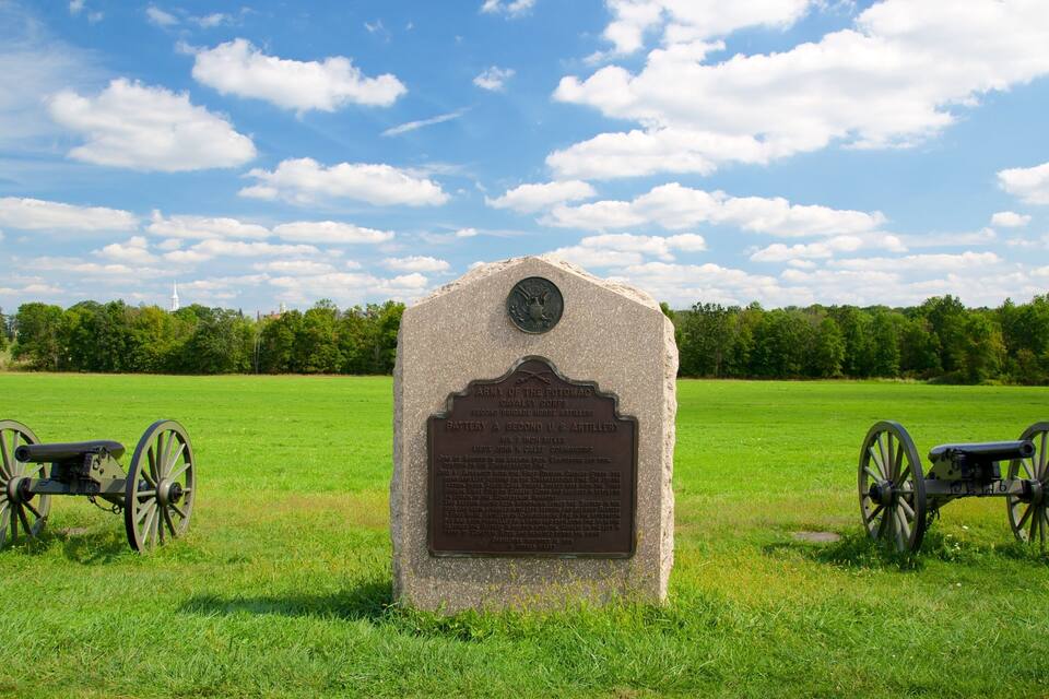 A historical marker with two cannons in a grassy field under a blue sky.