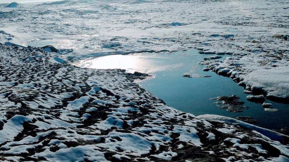 A snowy landscape with a frozen lake and distant mountains.