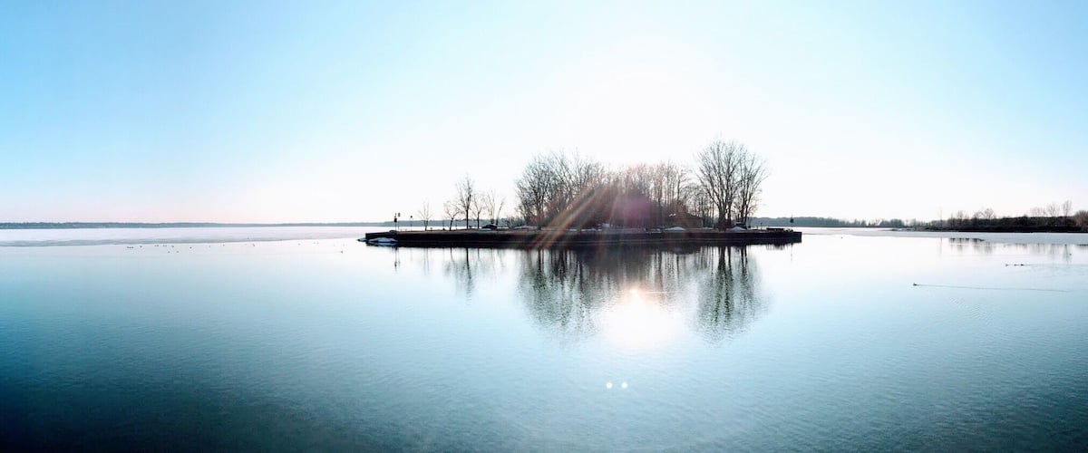A calm lake with a small island in the center, surrounded by trees and a clear sky.