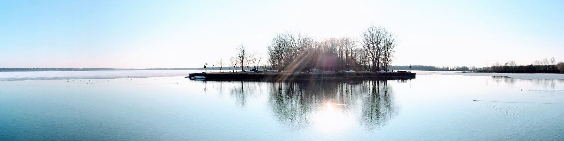A calm lake with a small island in the center, surrounded by trees and a clear sky.