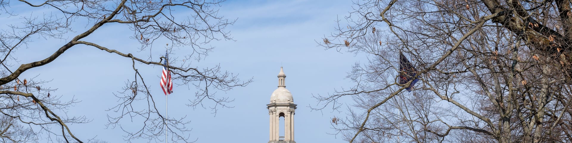A large building with a prominent tower and columns, surrounded by trees and a flagpole with an American flag.