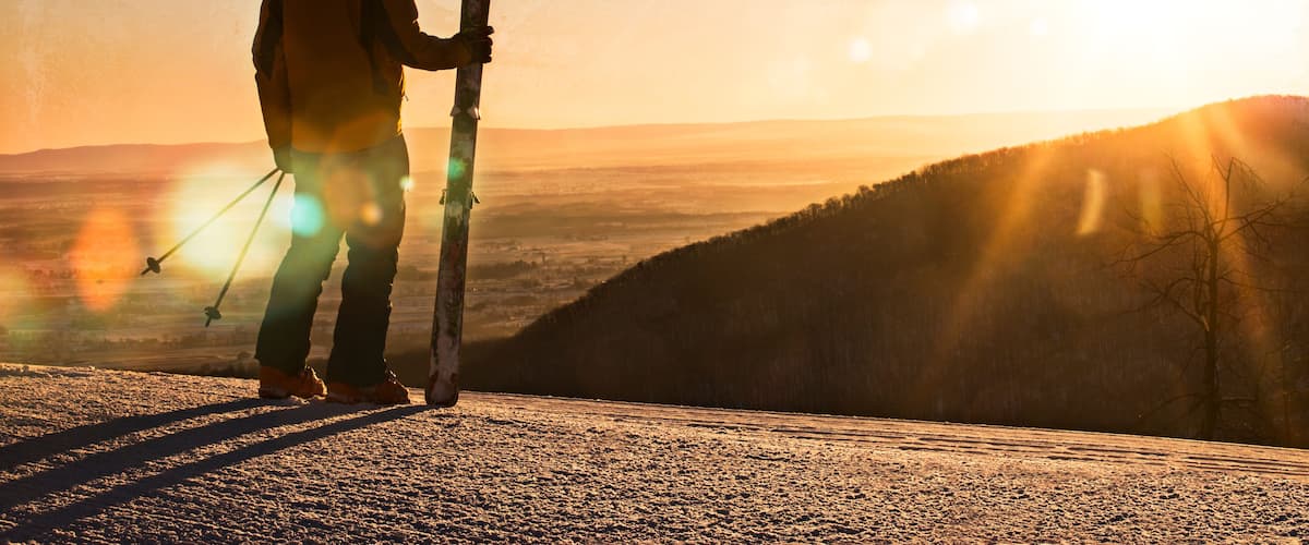 A skier stands on top of a mountain watching the sunrise in Pennsylvania.