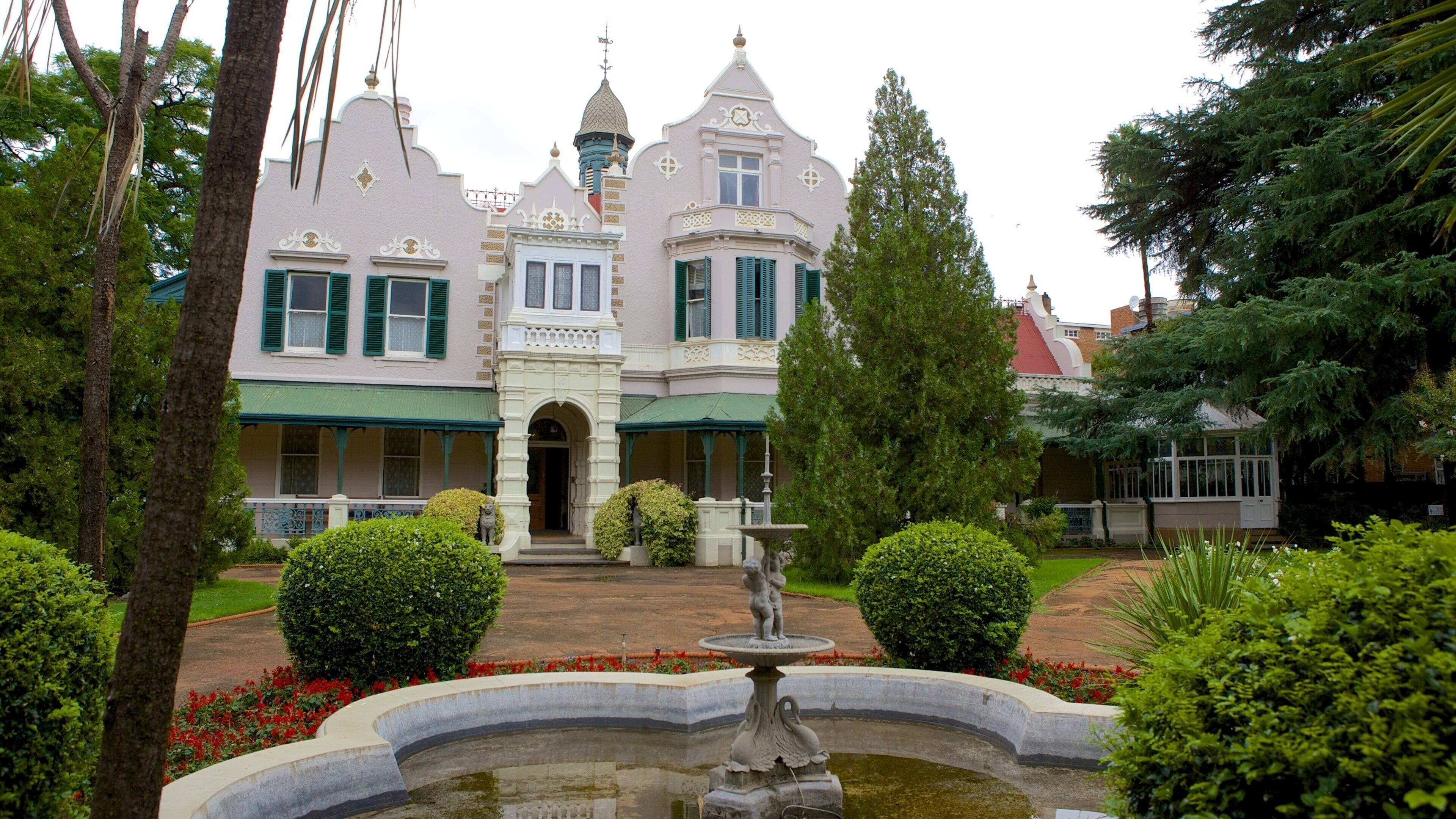 Un edificio histórico con arquitectura ornamentada, una fuente y jardines bien cuidados.