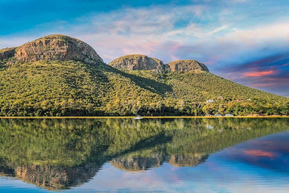 A calm lake with a boat, surrounded by green hills and a clear sky.