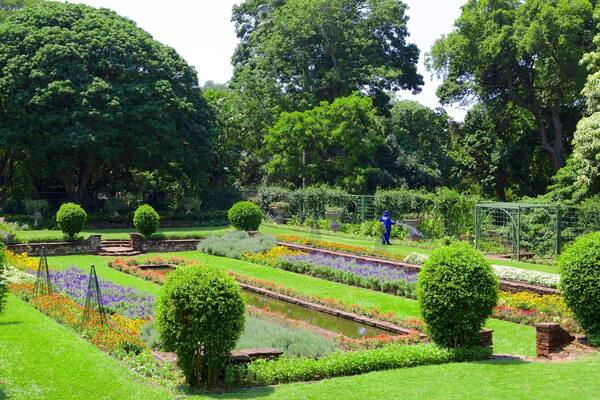 Un jardin bien entretenu, agrémenté de différents parterres de fleurs, de haies soigneusement taillées et d’un petit élément décoratif aquatique.