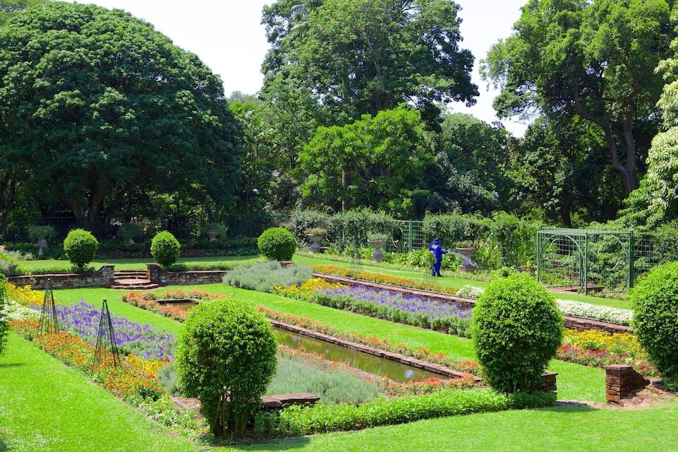 Un jardín bien cuidado con diferentes parterres de flores, setos podados con esmero y una pequeña fuente.