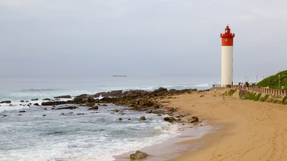 A beach with a lighthouse, rocky shoreline, and a ship in the distance.