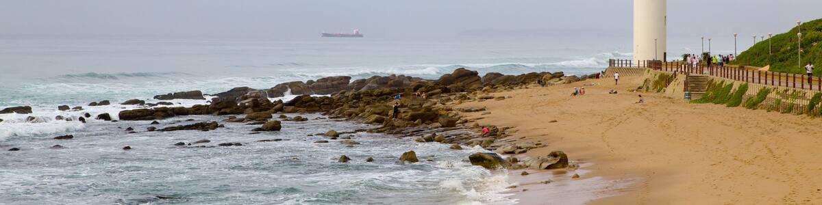 A beach with a lighthouse, rocky shoreline, and a ship in the distance.