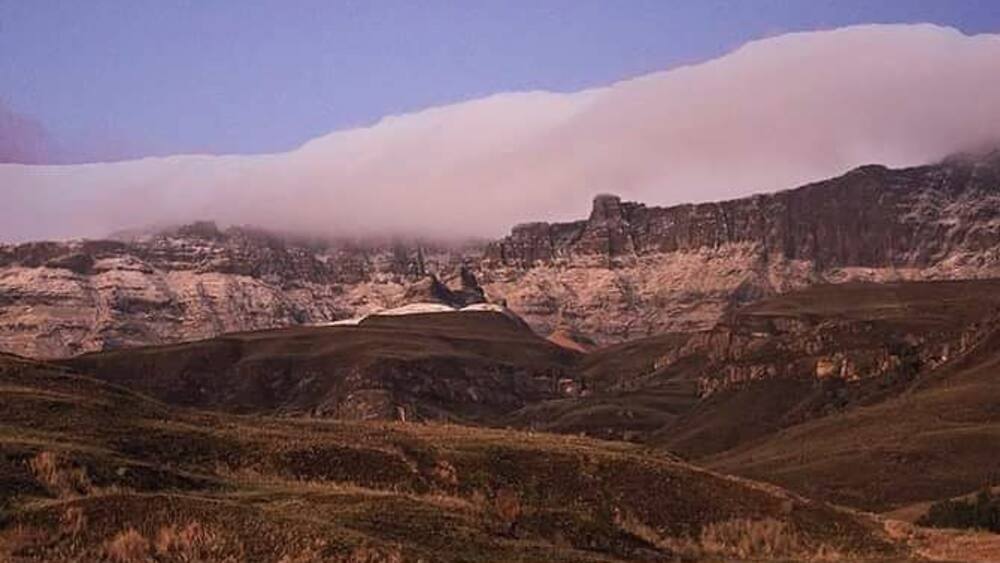 A mountainous landscape with a valley, a small settlement, and a cloud-covered peak.