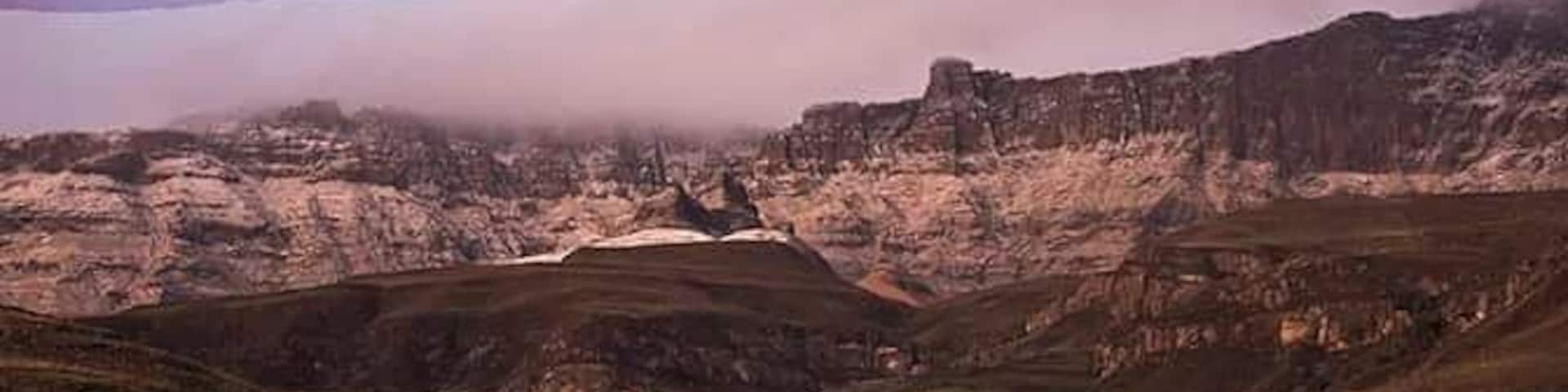 Paisagem montanhosa com um vale, um pequeno povoado e um pico coberto de nuvens.