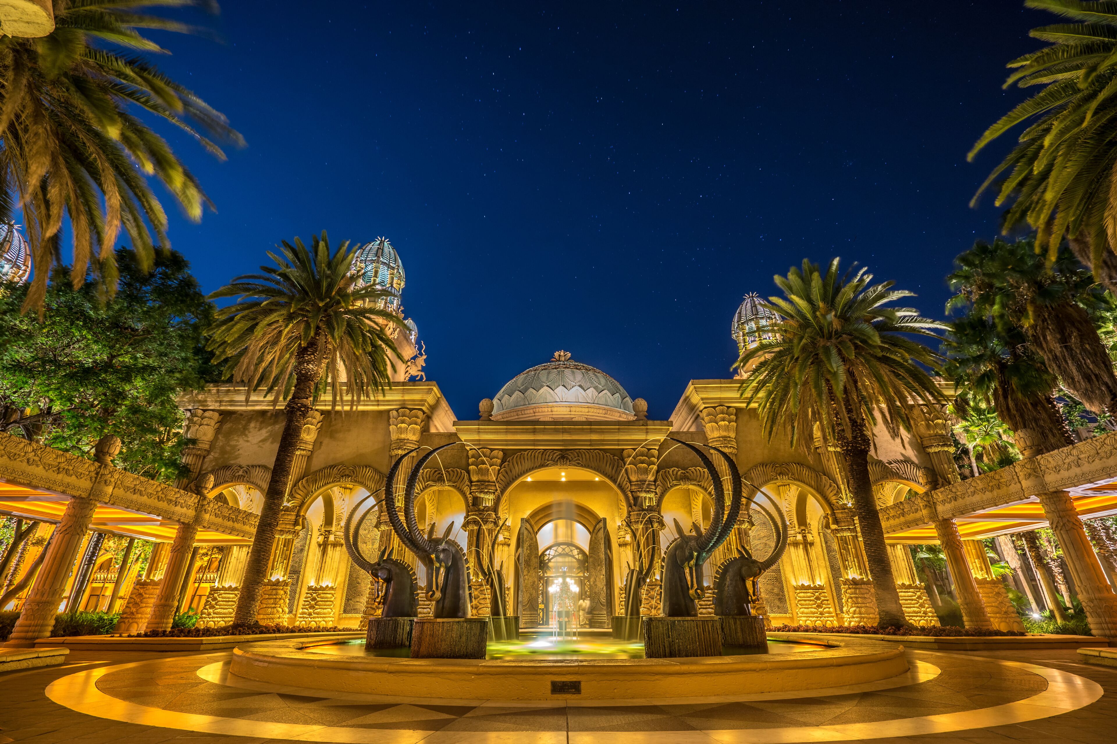 A grand architectural structure with domes and arches, surrounded by palm trees.