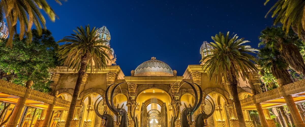 A grand architectural structure with domes and arches, surrounded by palm trees.