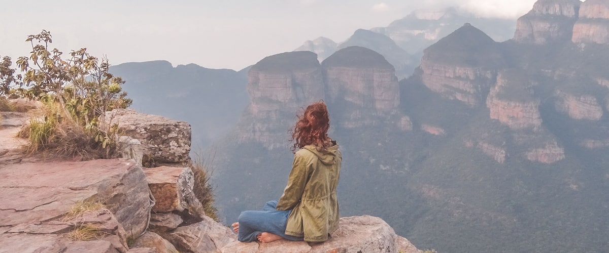 A person sitting on a rocky outcrop overlooking a canyon with layered rock formations.