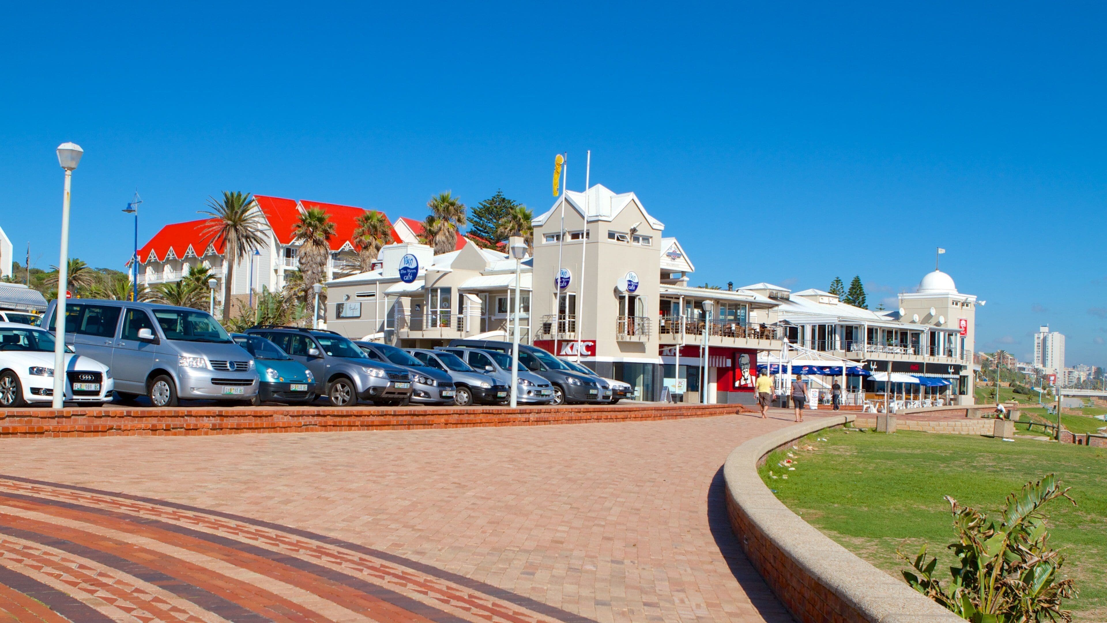 A parking lot with several cars, a building with a red roof, and a clear blue sky.