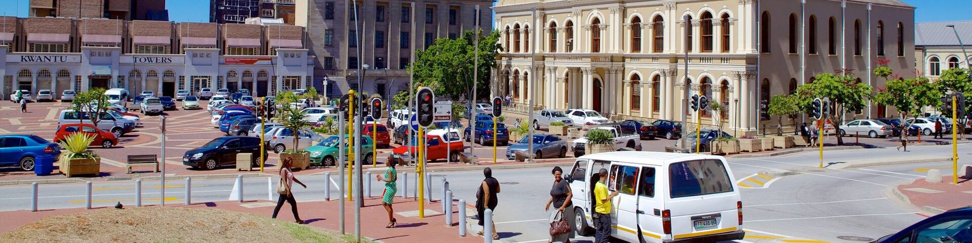 A city street with a prominent building with a clock tower, surrounded by various shops and vehicles.