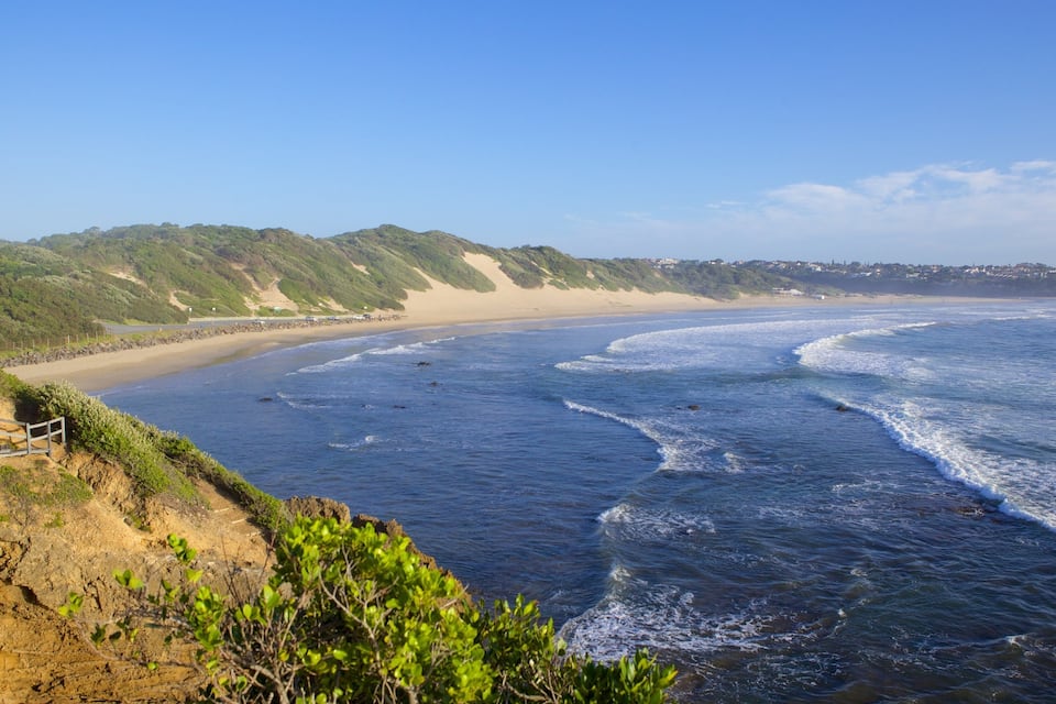 A coastal landscape with a sandy beach, rocky cliffs, and ocean waves.