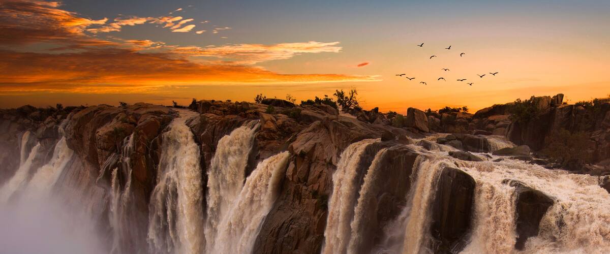 A waterfall cascading over rocky terrain during sunset.