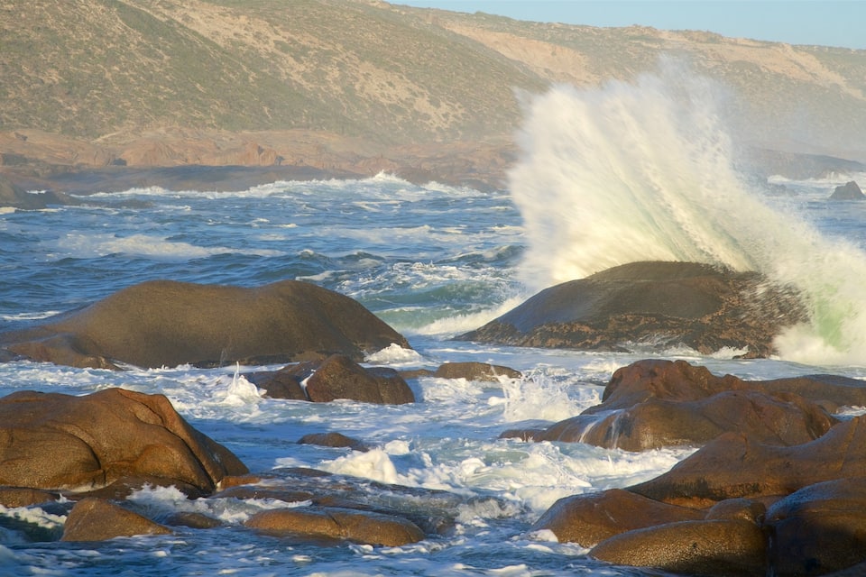 Costa rocosa con olas rompiendo contra grandes rocas y acantilados al fondo.