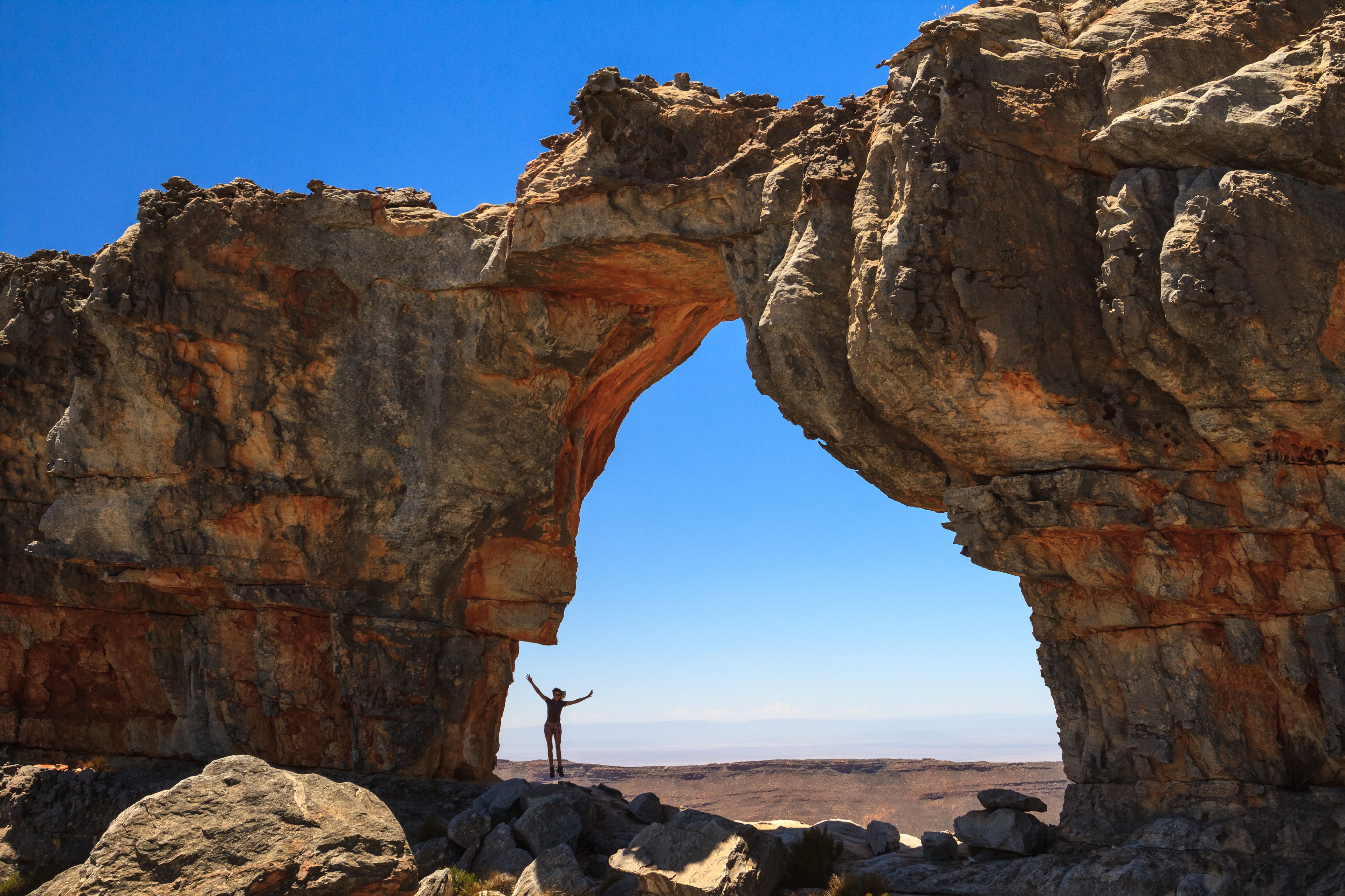 Une arche naturelle formée par des roches, avec une personne debout au premier plan.
