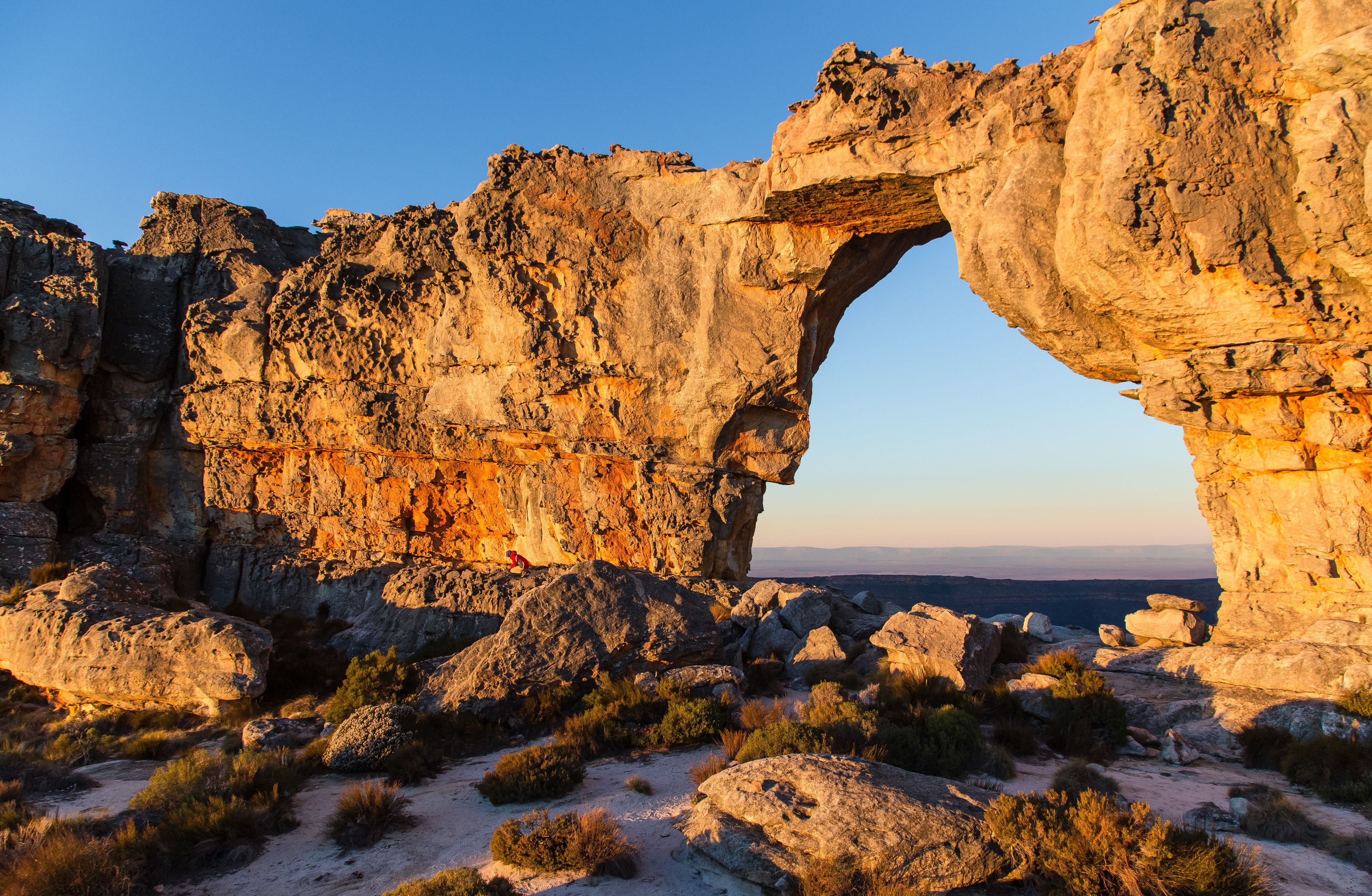Une arche naturelle formée par la roche, entourée d’une végétation désertique.