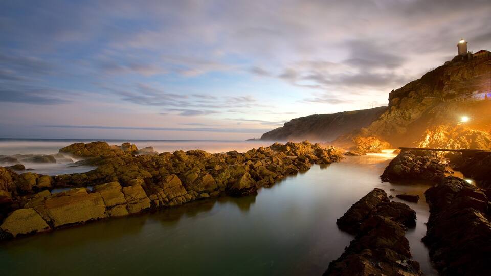 A rocky coastline with a lighthouse at sunset.