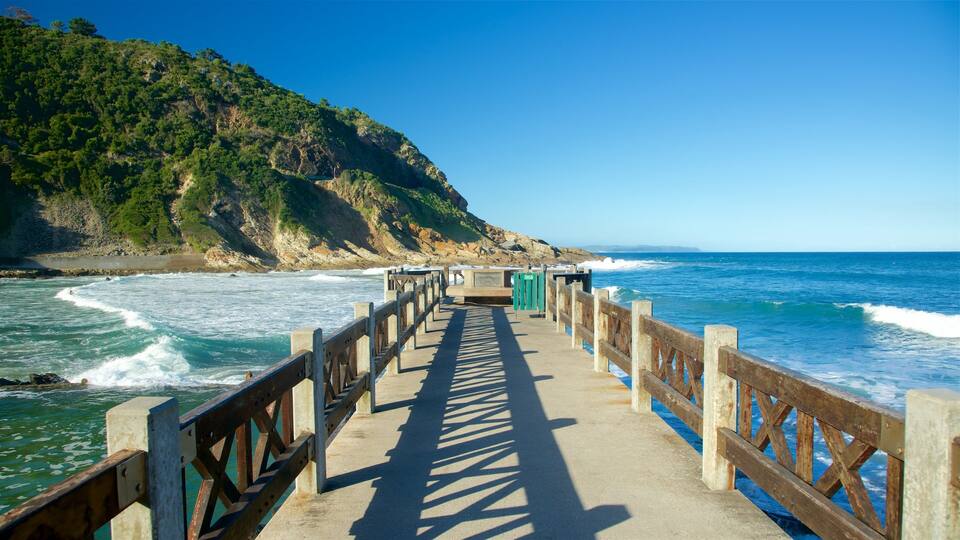 A wooden pier leading to a rocky coastline with waves crashing onto the shore.