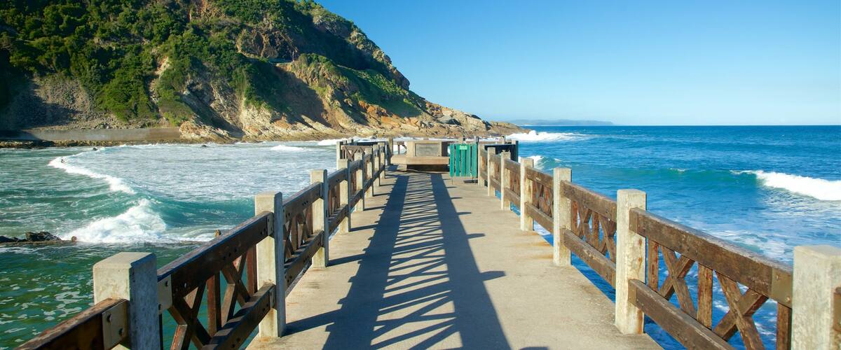 A wooden pier leading to a rocky coastline with waves crashing onto the shore.