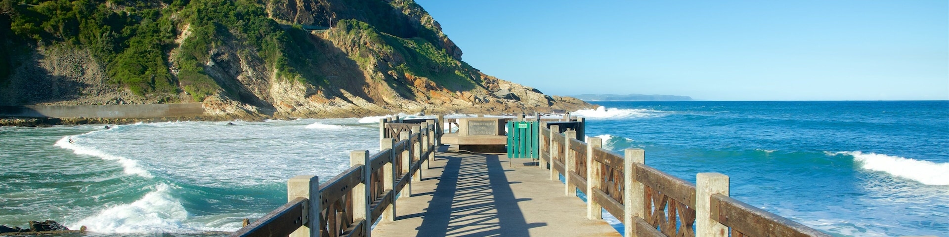A wooden pier leading to a rocky coastline with waves crashing onto the shore.