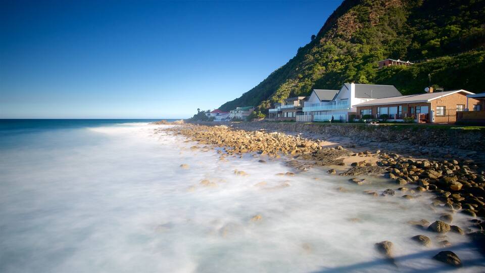 A beach with a rocky shoreline, houses, and a mountainous backdrop.