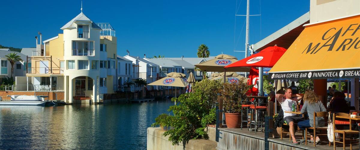 A waterfront café with outdoor seating, a canal, and a building with a tower.
