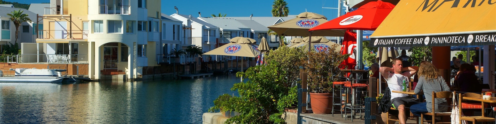 A waterfront café with outdoor seating, a canal, and a building with a tower.