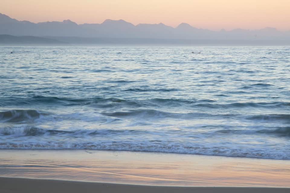 A beach with waves and mountains in the background.