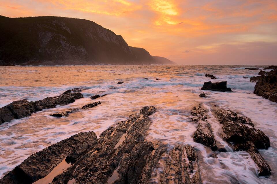 A rocky shoreline with waves crashing against the rocks during sunset.