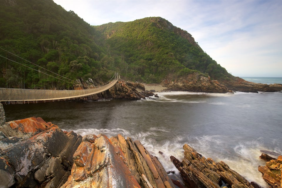 A suspension bridge over a river, surrounded by rocky cliffs and dense greenery.