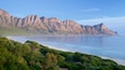A coastal landscape with rugged mountains and a calm sea.