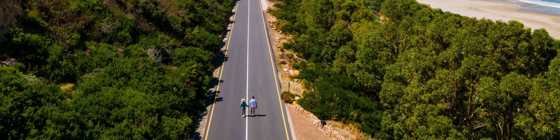 A coastal road flanked by dense greenery and mountains.