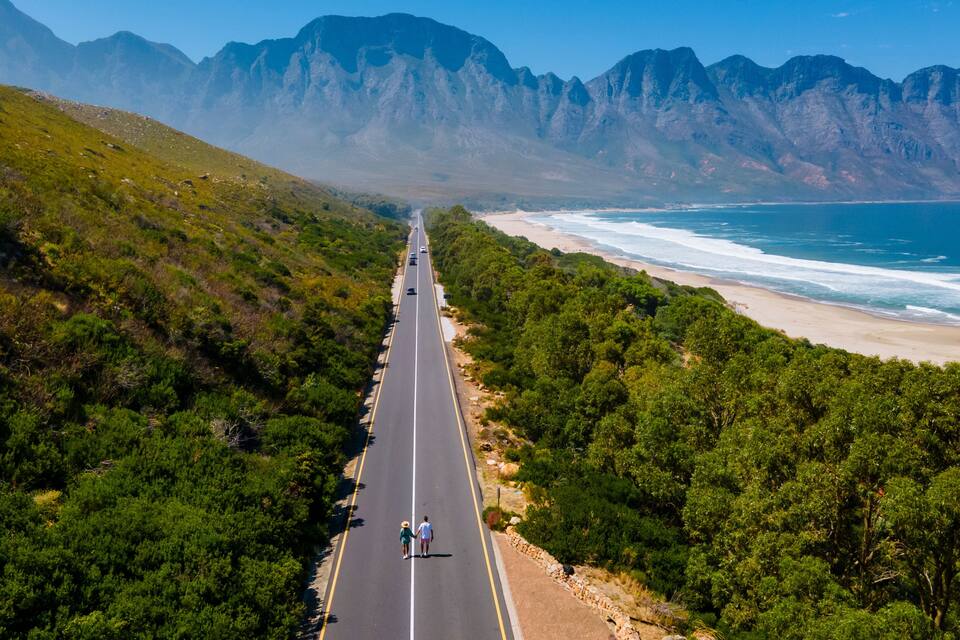 A coastal road flanked by dense greenery and mountains.