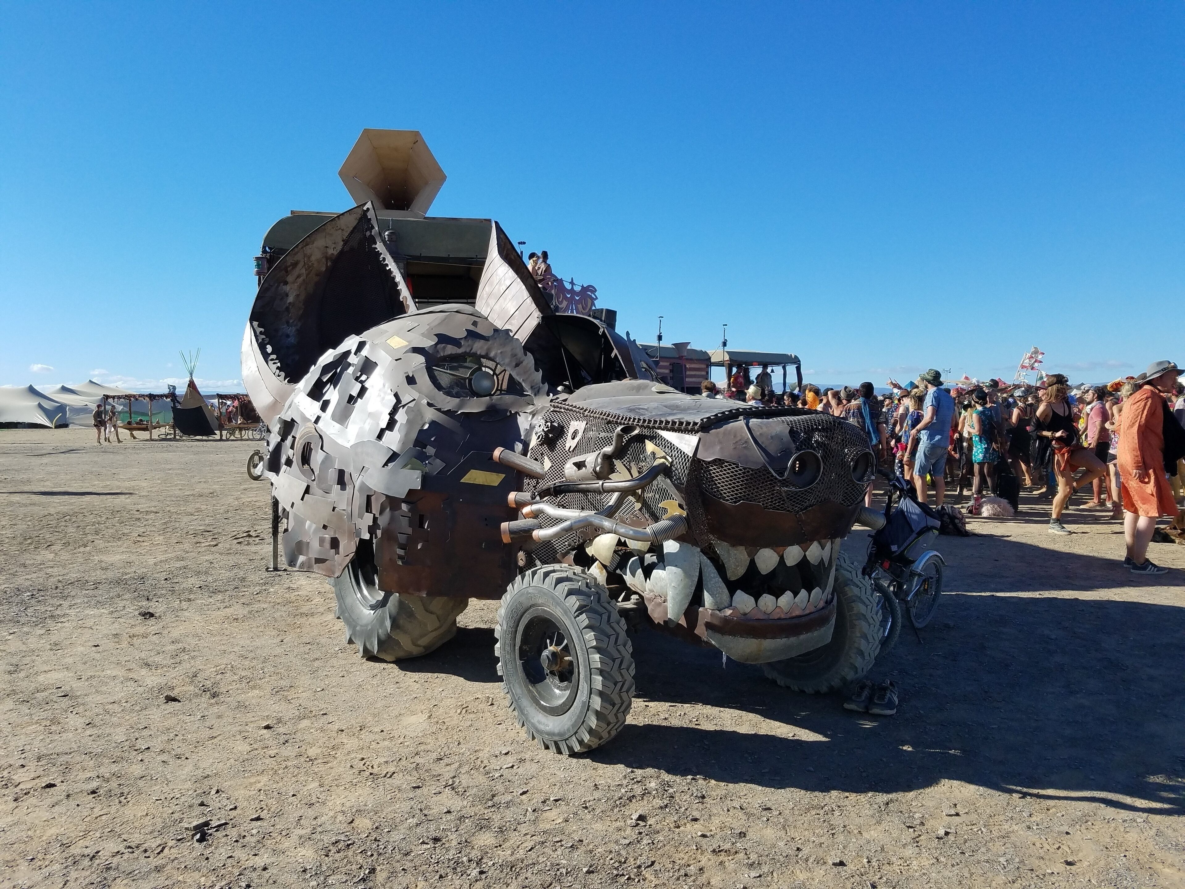 A large, decorated vehicle with a unique design, parked on a sandy area with people in the background.