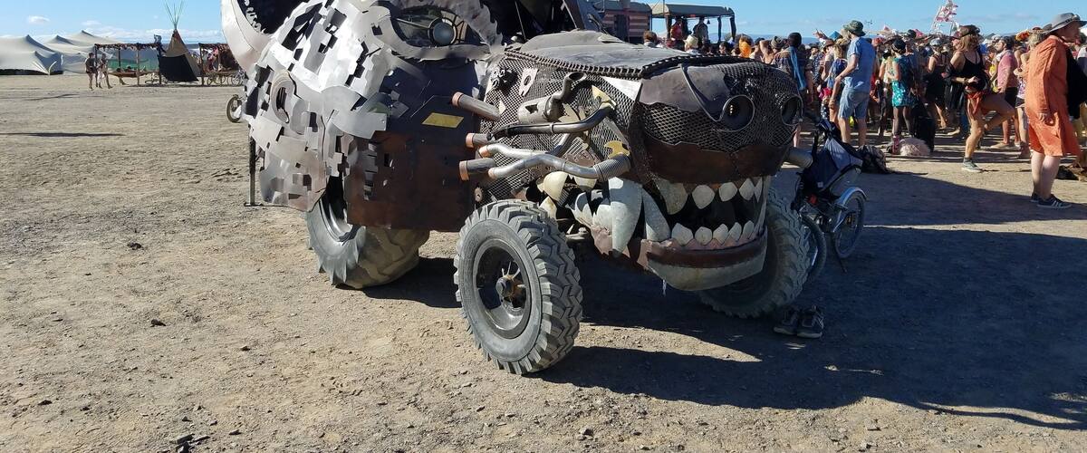 A large, decorated vehicle with a unique design, parked on a sandy area with people in the background.