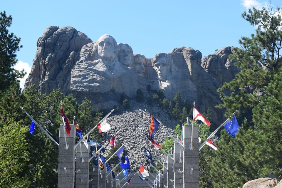 Mount Rushmore with flags and a stone monument in the foreground.