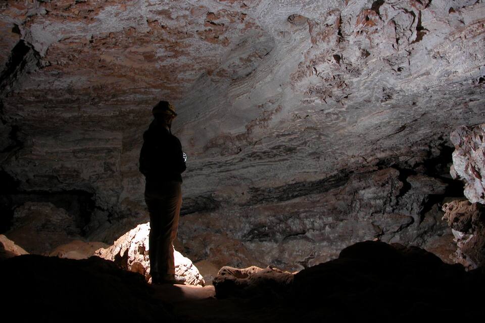 A person standing in a cave with rough, uneven walls and a rocky floor.