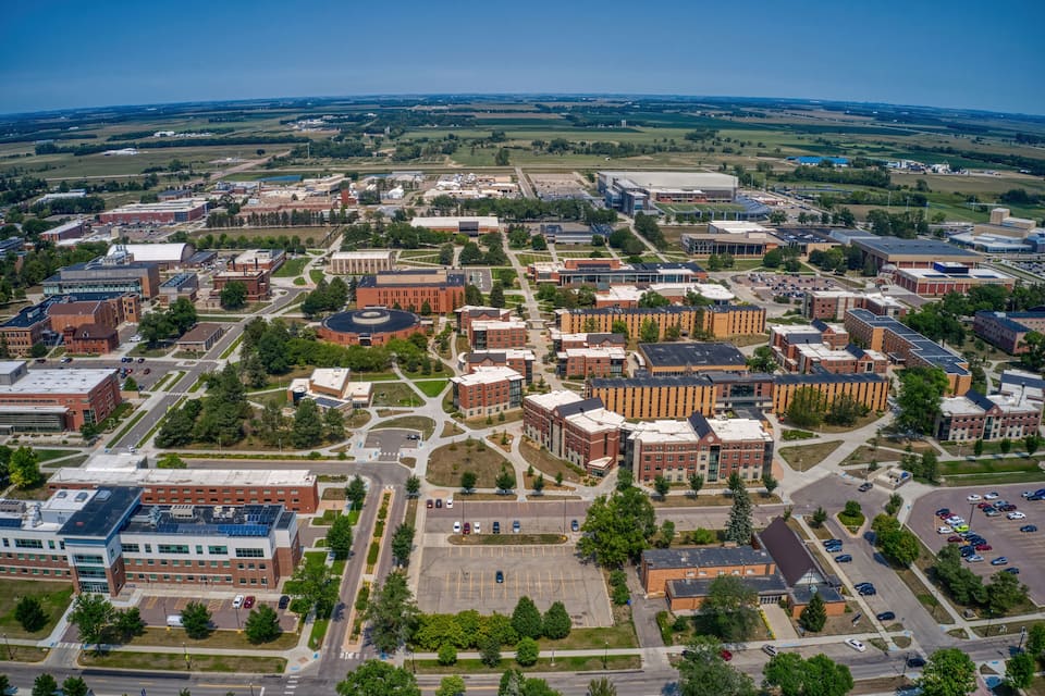 Vista aérea de un campus universitario con varios edificios, estacionamientos y zonas verdes.