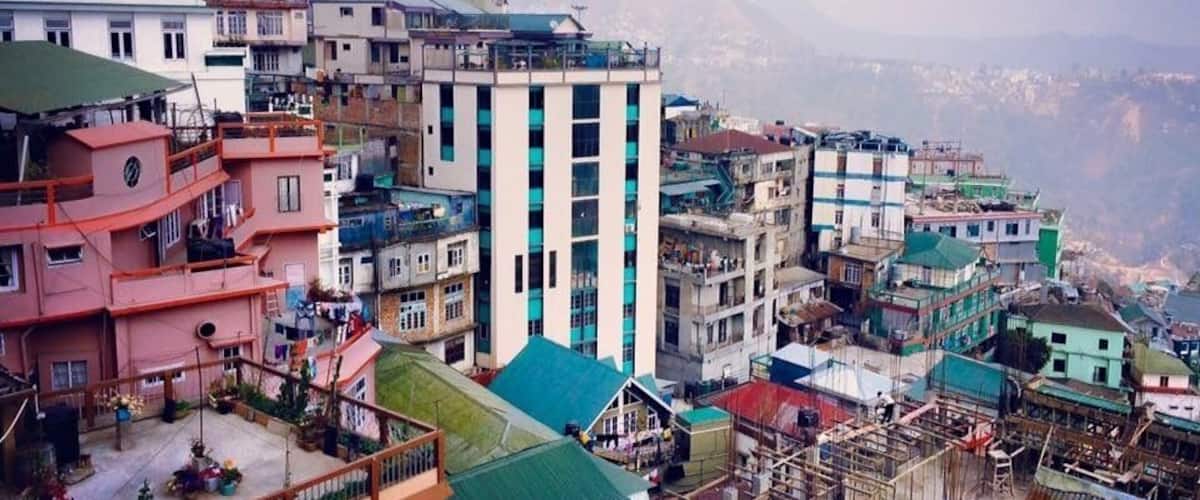 A densely packed urban area with multi-story buildings, some with balconies, and a mountainous backdrop.