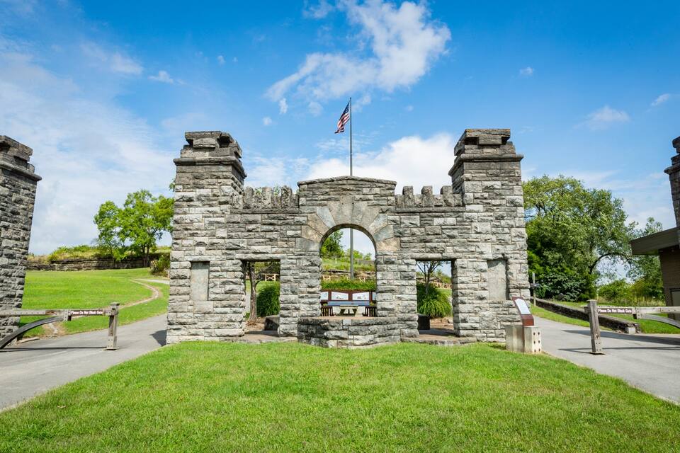 A stone castle with an American flag, surrounded by a grassy area and trees.